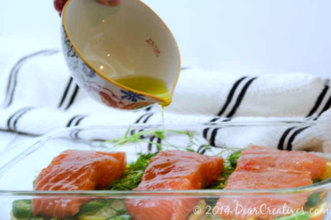 Olive oil being poured over salmon in a baking dish_DearCreatives.com