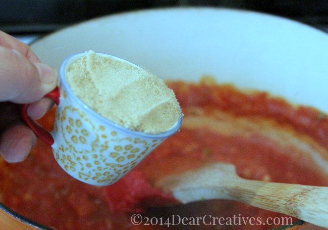 hand adding quarter cup brown sugar to barbecue sauce