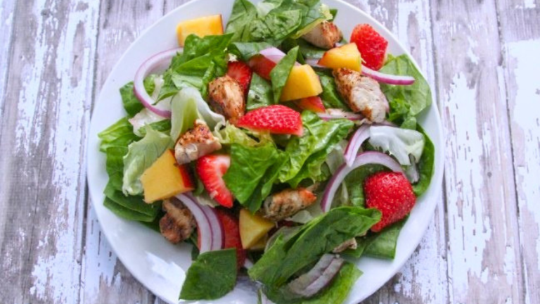 Easy grilled chicken salad with ginger dressing, strawberries, lettuce, and red onion served on a plate