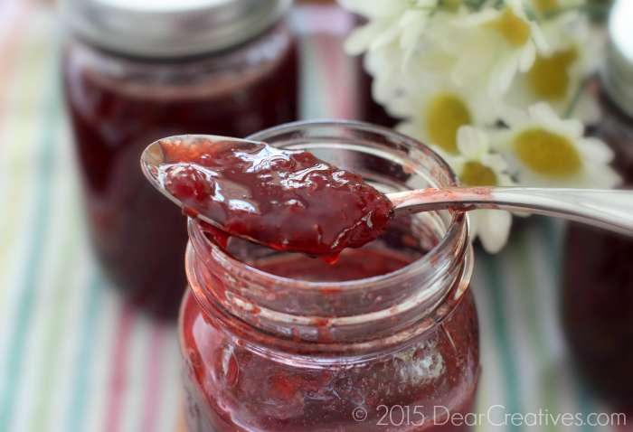 Strawberry Jam Recipe Strawberry jam on a spoon sitting on top of a mason jar full of jam