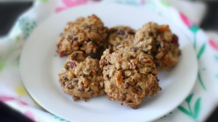 Oatmeal breakfast cookies on a plate with dried fruits, oatmeal, and other healthy ingredients. The plate is sitting on top of a pretty kitchen towel to keep the warm cookies from damaging the table.