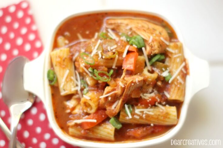 close up of a bowl of chicken cacciatore ready to eat with a fork, spoon, and napkin that is red and white