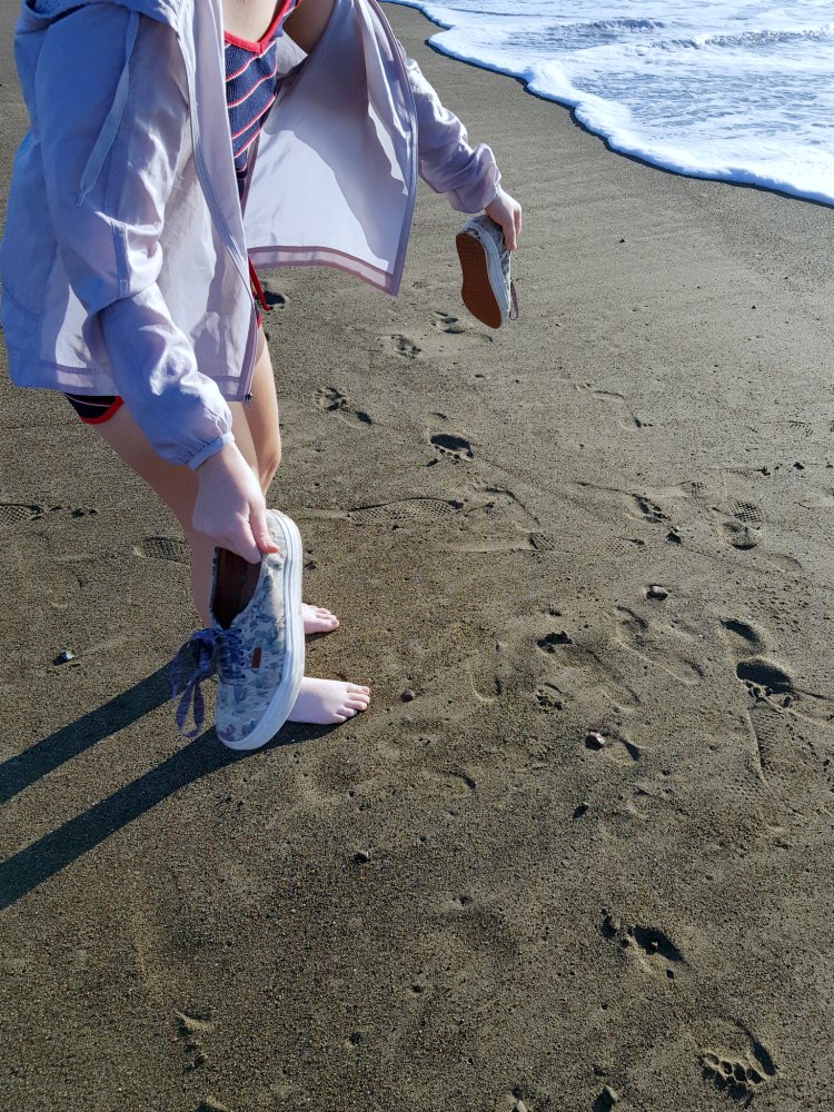 knocking the sand off tennis shoes at the beach to put into a bag