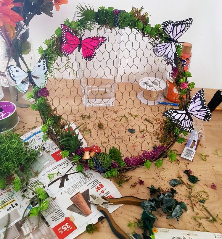 finishing touches to a grapevine wreath with chicken wire with succulents, moss, butterflies, and mushrooms. See how to decorate a wreath at DearCreatives.com