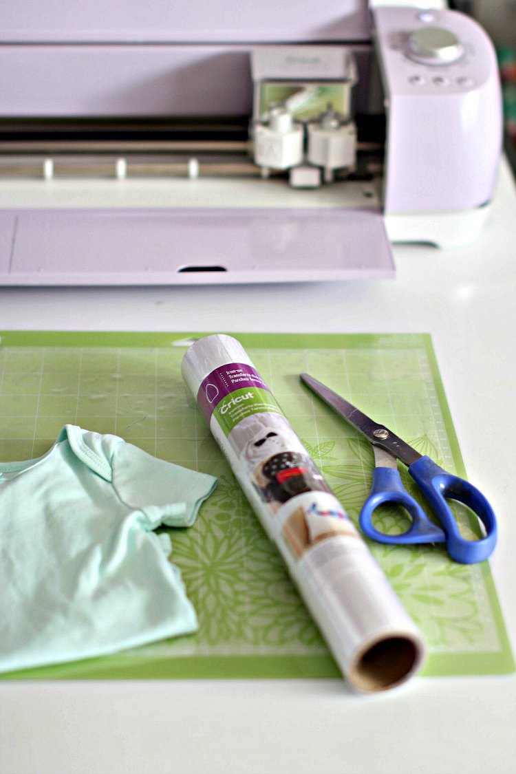 Cricut cutting machine, iron on material, baby onsie, scissors, and cutting mat to make iron on onsies DearCreatives.com