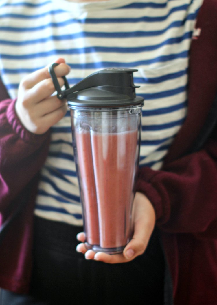 Holding a smoothie in a to go cup with a ring on the lid for attaching to backpacks or bags to take when on the go. DearCreatives.com