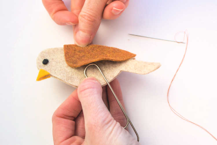 Securing the paper clip under the wing of the felt bird. Find this diy felt bookmark and more at DearCreatives.com