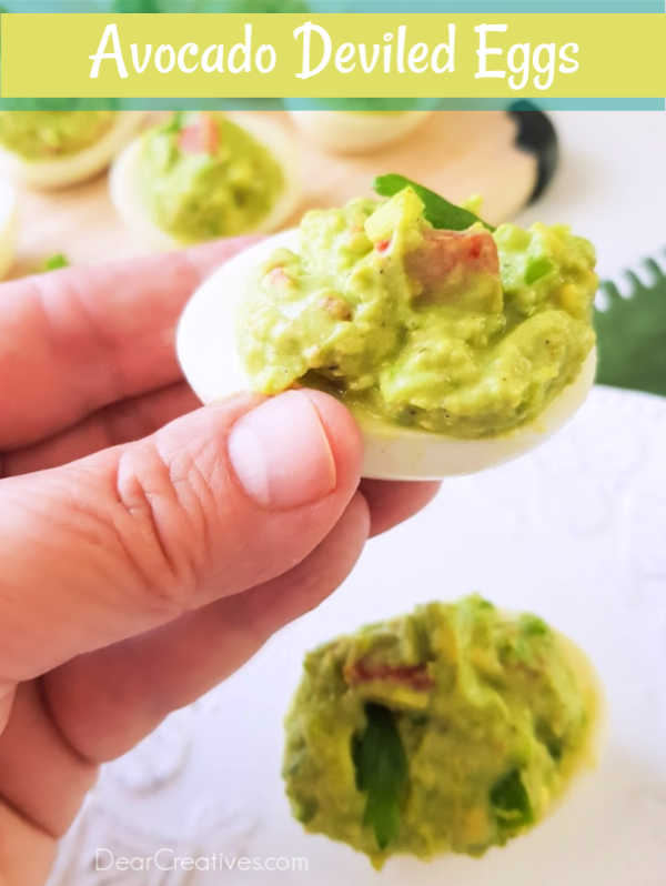 Avocado Deviled Eggs - holding a avocado deviled egg in hand - Grab this avocado deviled egg recipe to make guacamole deviled eggs. This appetizer recipe for the win! DearCreatives.com #avocadodeviledeggs #guacamoledeviledeggs #deviledeggsrecipe #avocado #guacamole #deviledeggs #appetizers #recipe