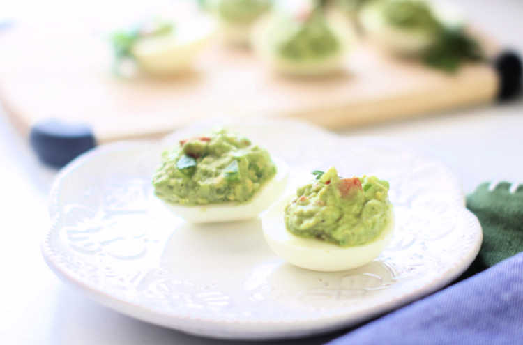 transferring guacamole deviled eggs onto serving plate after making them. Recipe at DearCreatives.com