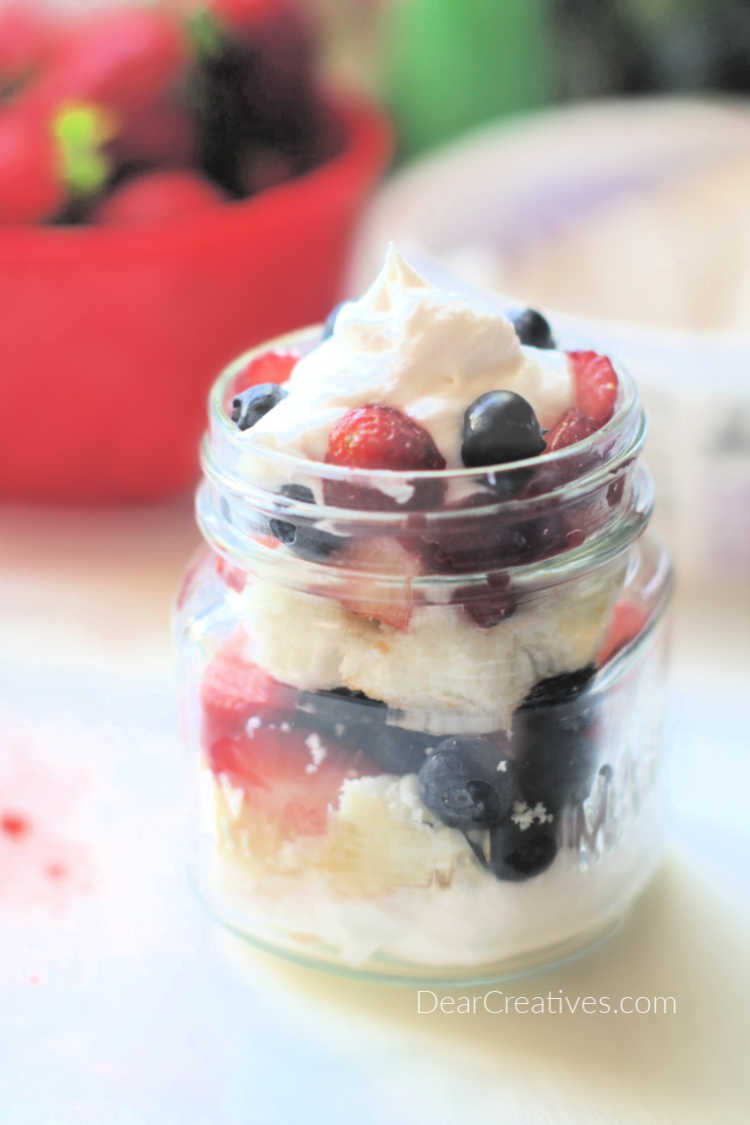 Adding the final whip cream and berries to the mason jar no bake dessert. DearCreatives.com