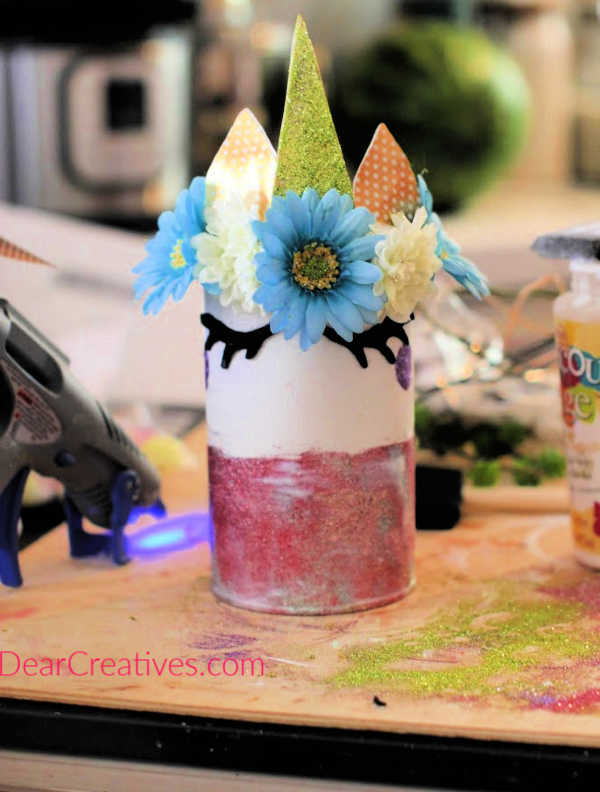 Cut out unicorn felt eyes or purchase them and add them to your unicorn can or jar with a hot glue gun or strong glue. Full instructions at DearCreatives.com