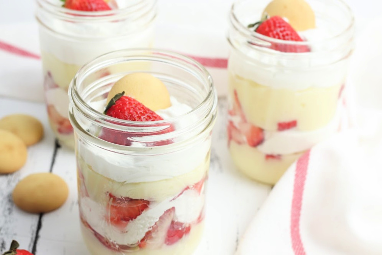 Topping the strawberry trifle in mini mason jars. See how to make this easy no-bake dessert at DearCreatives.com