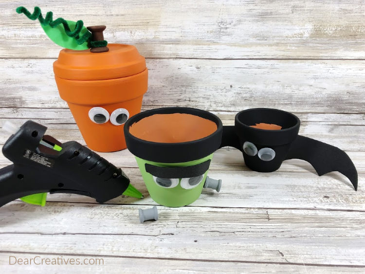 Attach all features to clay pots with a glue gun and glue sticks. Use photo for placement. Step 5 of the step by step instructions with images for making a Frankenstein, Jack-O-Lantern and a Bat from clay pots
