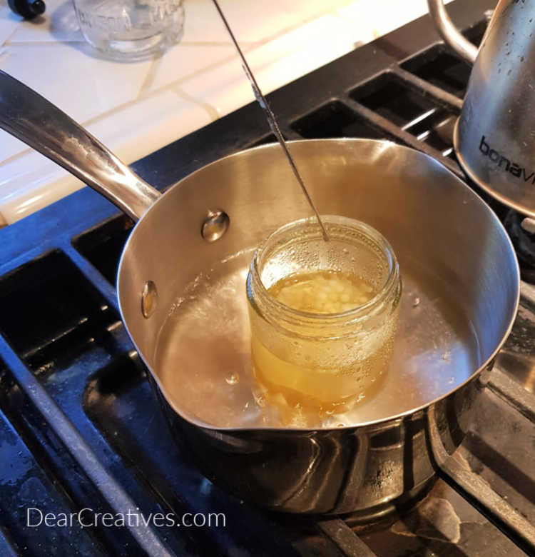 Melting beeswax in a jar on the stove in a pot of water to make lip balm DIY LIP BALM - how to and recipe at - DearCreatives.com