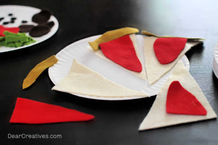 We cut out these felt shapes by hand. We made templates for the pizza toppings and pizza. They are free printables for making the felt pizza. Find instructions and template at DearCreatives.com