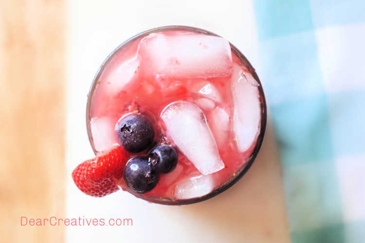 strawberry iced tea - looking close up top down with garnishes of strawberries and blueberries. Get this delicious pink drink recipe at © DearCreatives.com 