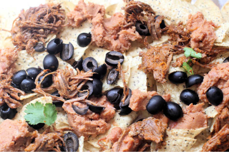 adding pre-cooked beef, beans, olives...onto corn tortillas to make nachos - © DearCreatives.com