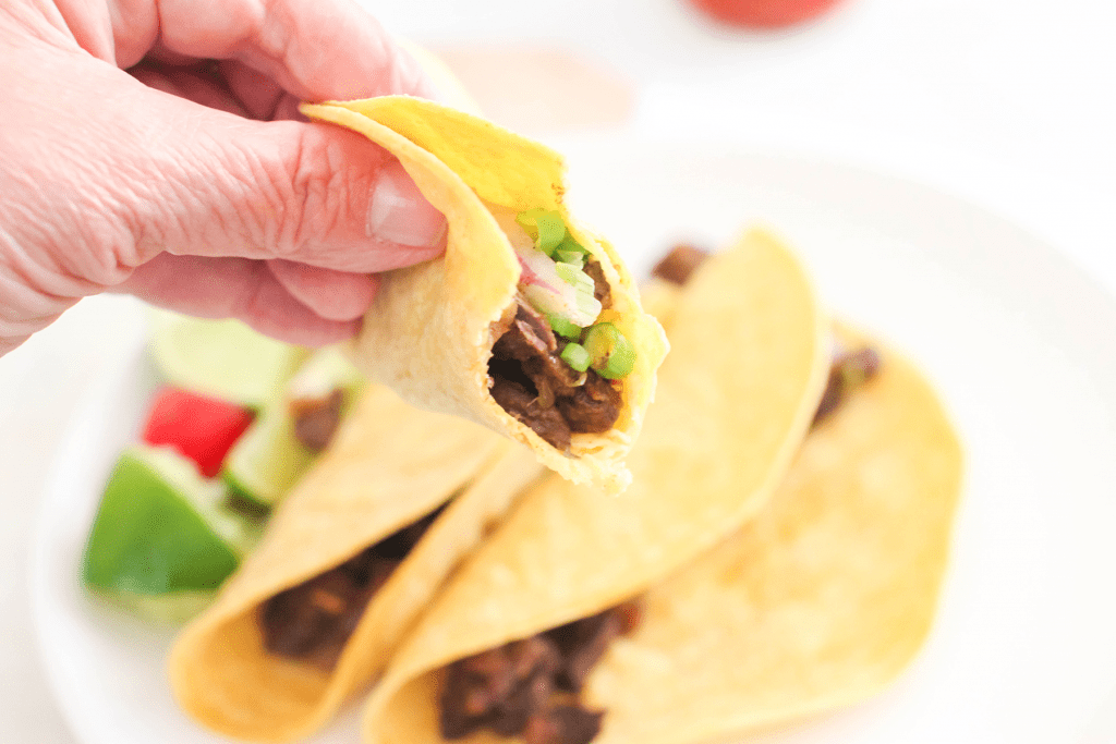 Carne Asada Tacos-being-held-with-a-bite-taken-Grab-the-steak-tacos-recipe-at-©-DearCreatives.com