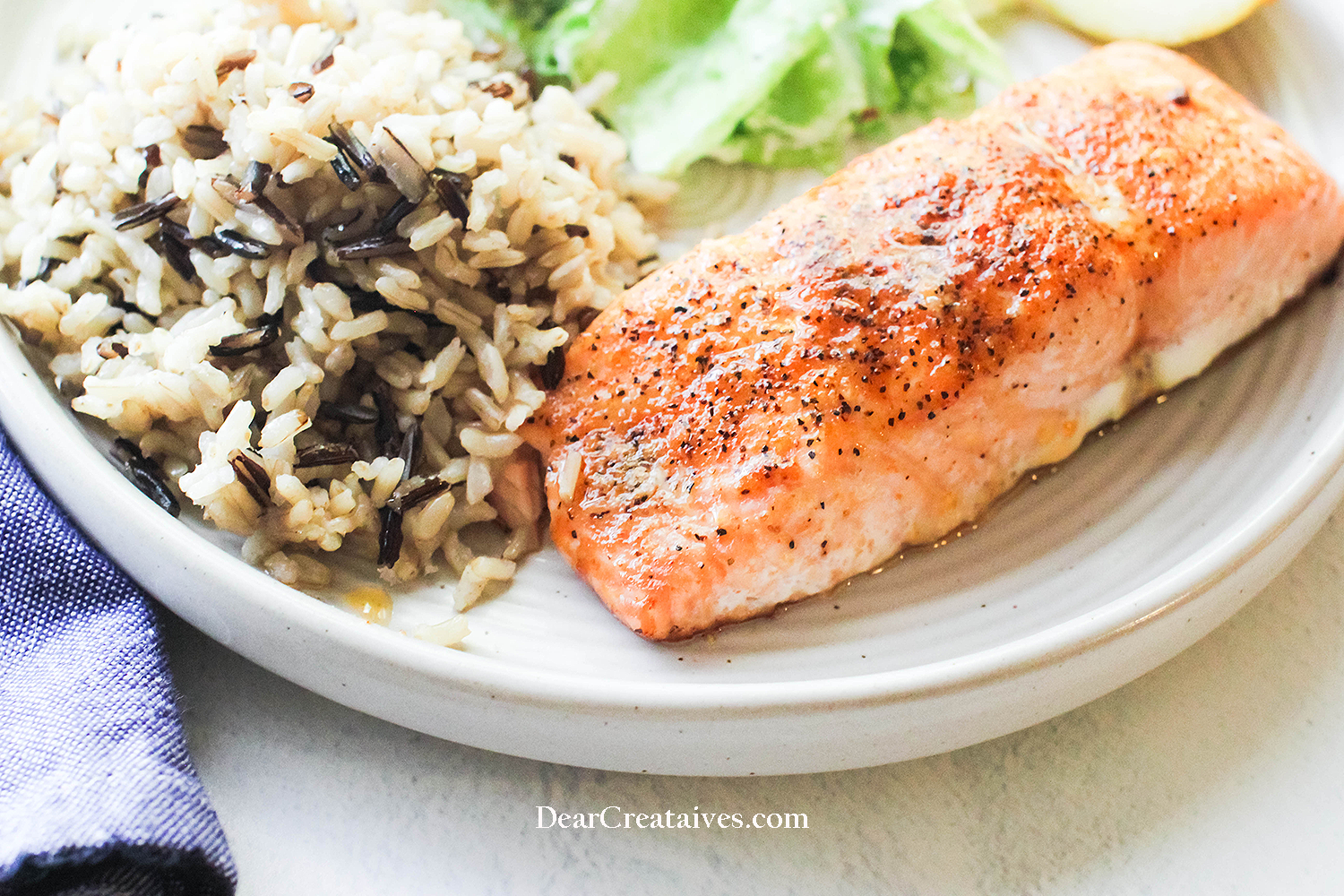 Close up of baked salmon on a plate with wild rice and a salad - Recipe for salmon at © DearCreatives.com