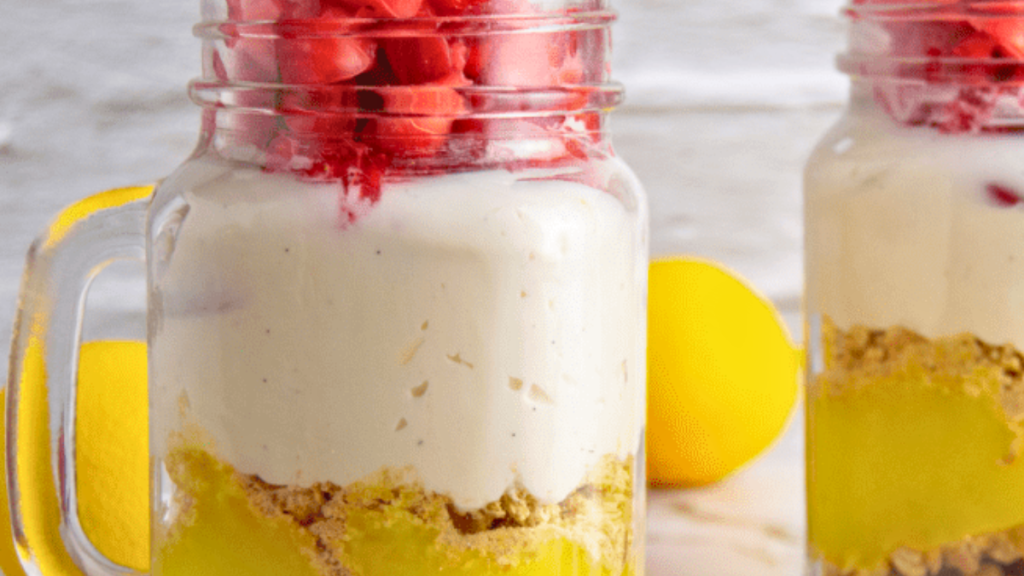 no bake strawberry lemon dessert  closeup of two jars of the strawberry lemon mason jar dessert with lemons in the background