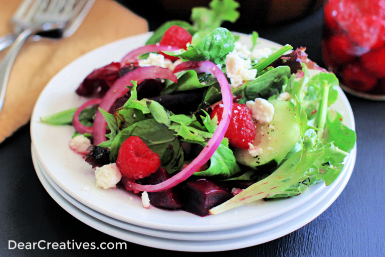 Mixed Greens With Homemade Raspberry Vinaigrette Dressing it has red onion, raspberries, crumbled cheese on top of a bed of mixed green salad ©2023 DearCreatives.com