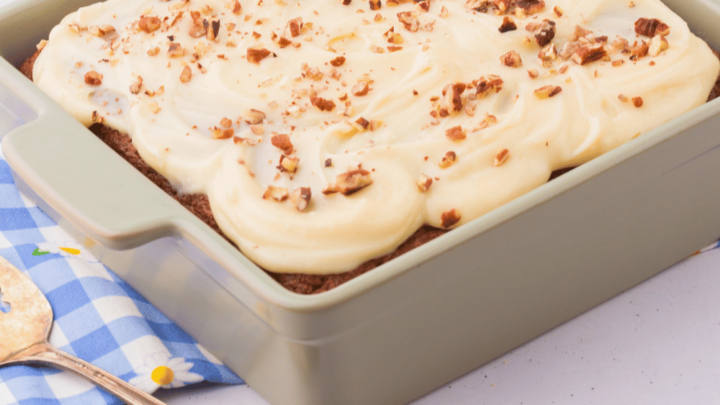 Fully assembled easy banana cake in an 8×8 pan topped with cream cheese frosting and garnished with chopped pecans