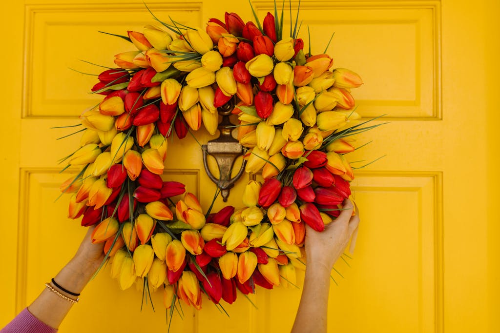 Colorful tulip wreath held by hands on a yellow door, perfect for spring decor.