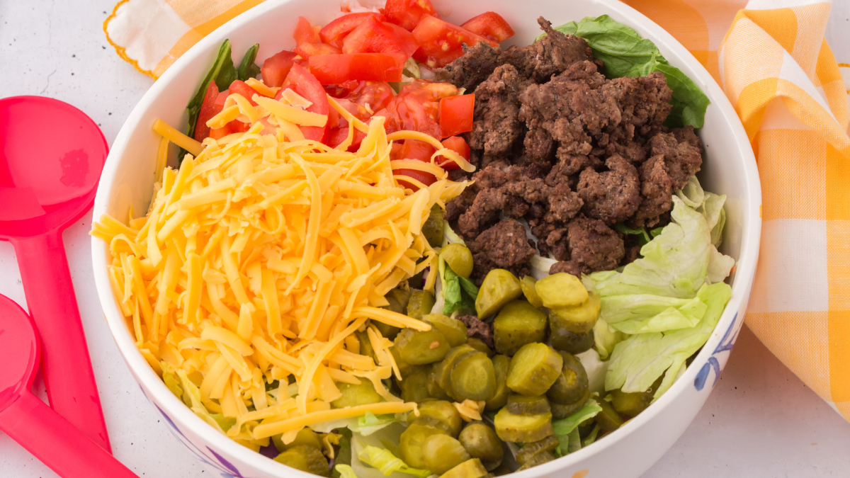 Prepared salad with lettuce, tomatoes, shredded cheddar cheese, pickles, and ground beef. Ready to add the special dressing to make the Big Mac Salad. DearCreatives.com