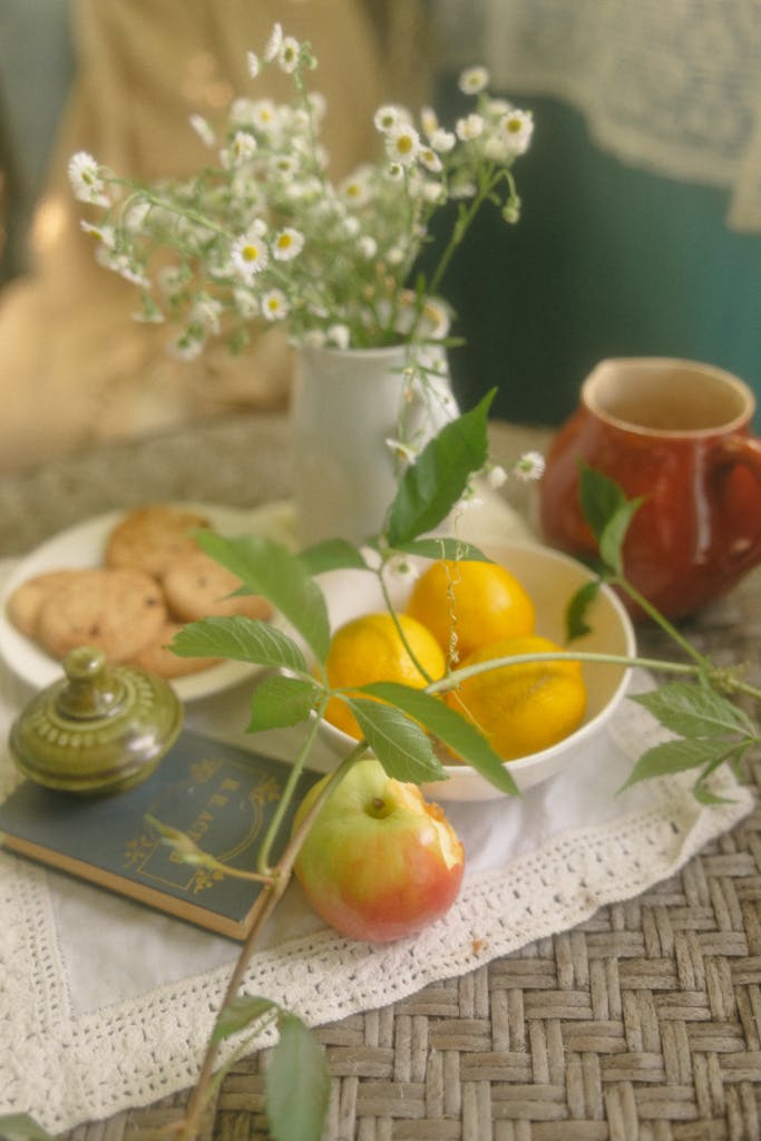 A cozy still life of apples, lemons, cookies, and daisies in warm, soft tones.