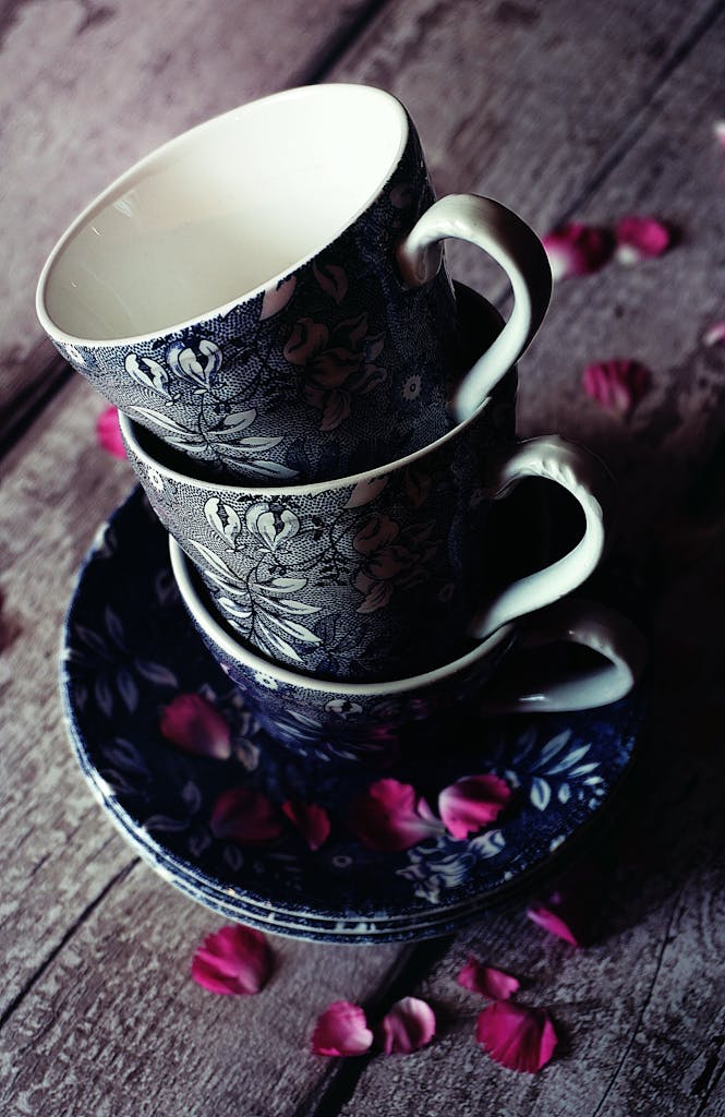 Cottagecore Vintage floral teacups stacked with rose petals on a rustic wooden table. Elegant and timeless.