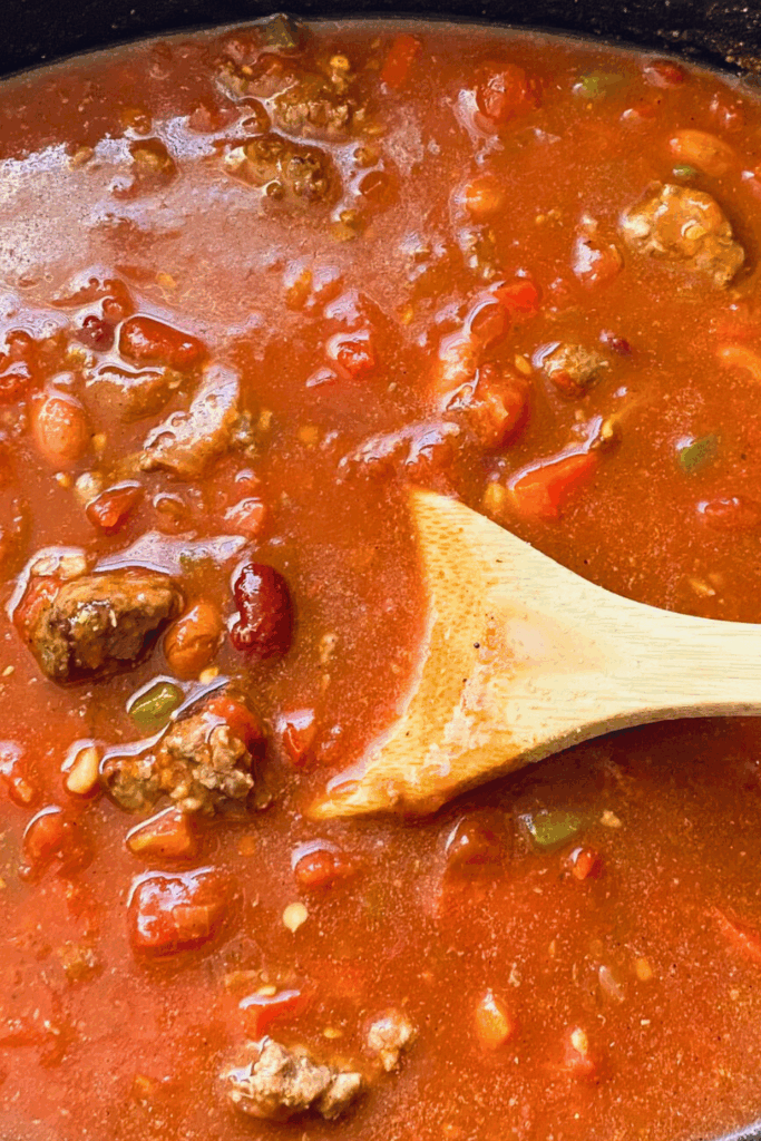 Hearty Chili close up in a slow cooker with ground beef and beans in a tomato sauce with peppers, onion, garlic, herbs and spices. 