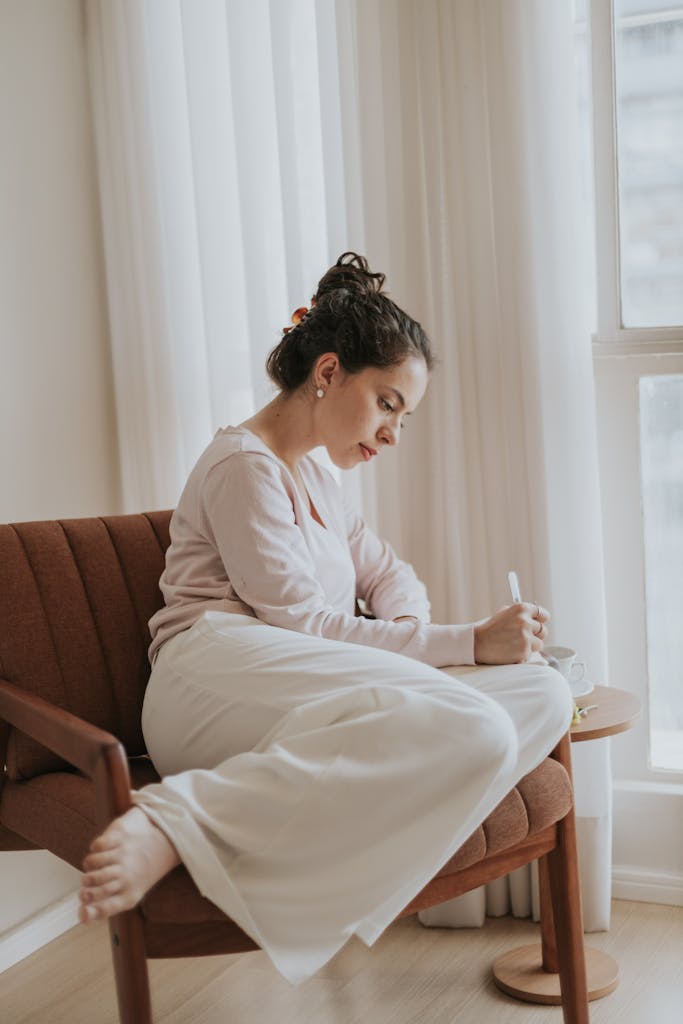 A woman enjoying a peaceful moment journaling while sitting in a cozy chair by a window.
