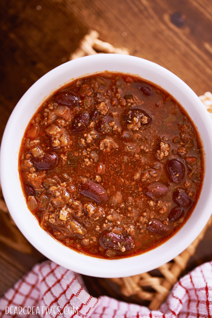 chili with ground beef, kidney beans, chili beans, onion, garlic, spices served in a bowl, hearty, warm, and comforting looking.