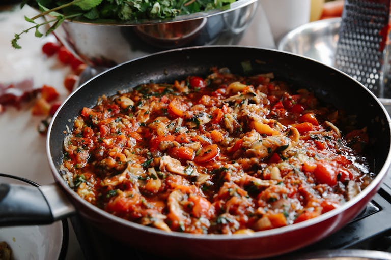 Close-up of a vibrant pasta sauce with vegetables dish cooking in a pan, featuring tomatoes and herbs.