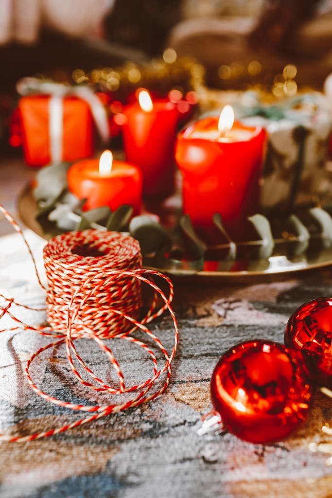 Cozy Christmas scene with red candles, red ornaments, and gifts on a table.