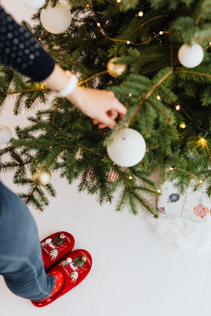 Person decorates Christmas tree with baubles, wearing festive red slippers. Cozy holiday vibe. Using neutrals and affordable Target Christmas decor...