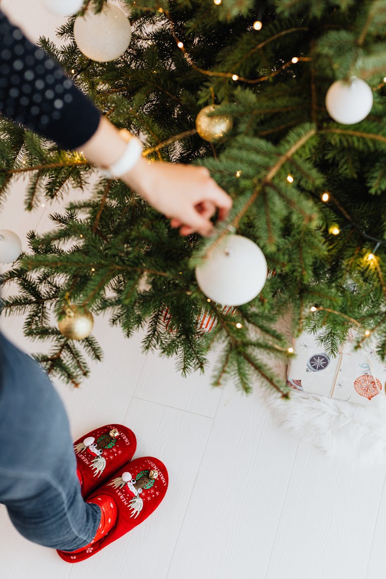 Person decorates Christmas tree with baubles, wearing festive red slippers. Cozy holiday vibe. Using neutrals and affordable Target Christmas decor...