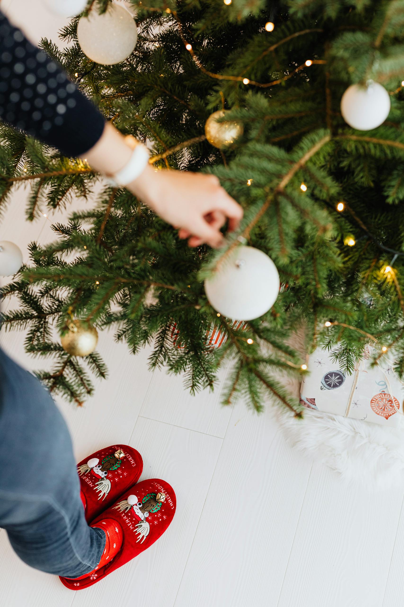 Person decorates Christmas tree with baubles, wearing festive red slippers. Cozy holiday vibe. Using neutrals and affordable Target Christmas decor...