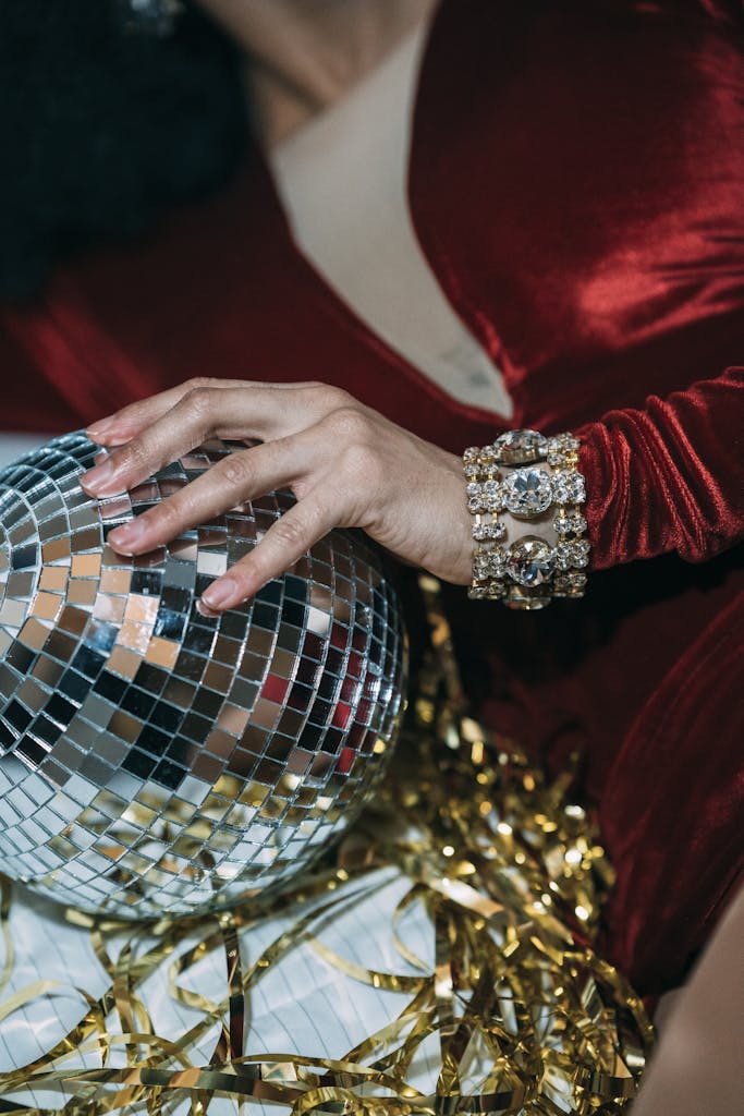 Crop unrecognizable female in bright red dress either satin or velvet, and jewelry maybe lying and reaching for with disco ball and tinsel. Festive, Cherry Red Aesthetic