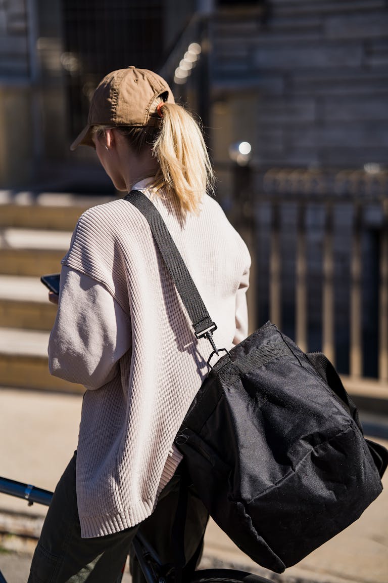 A young woman with a cross shoulder gym bag walking outdoors and on the phone while heading to the gym.