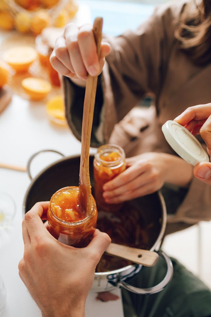 Closeup image o canning with hands on jars and adding jam to the jars. Preparing homemade jam in glass jars. In a home kitchen setting.