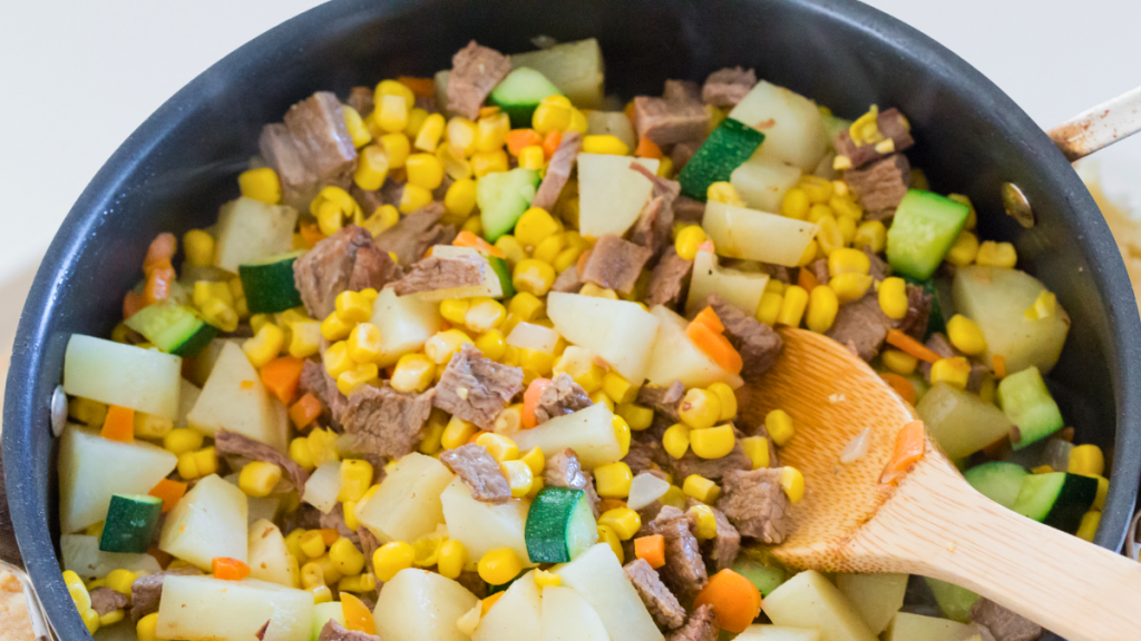 Beef, potatoes, corn, and vegetables sautéing together in a pan to make the filling for homemade beef pot pie.