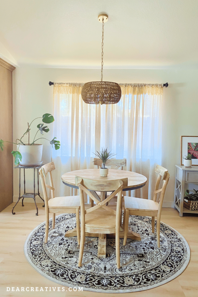 Bright coastal dining room with airy linen curtains, round wood dining table, woven round rug, and rattan pendant light creating a relaxed summer home style - DearCreatives.com