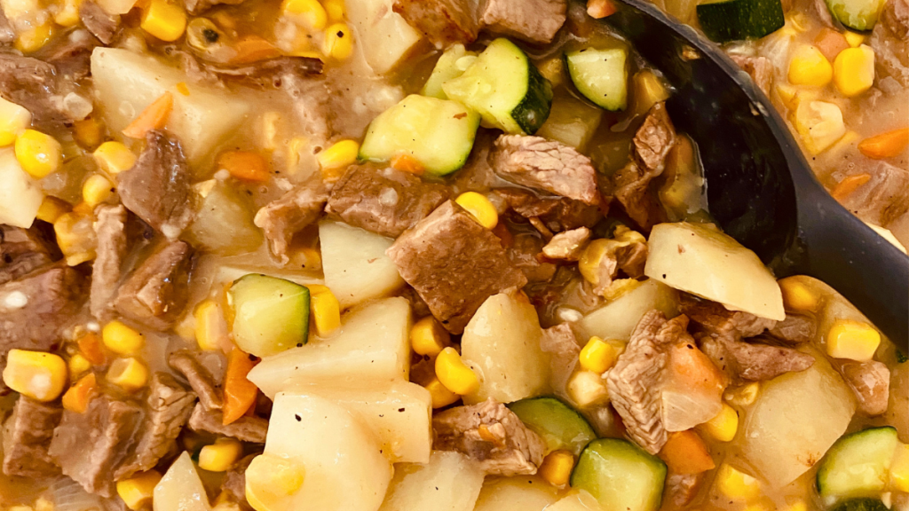 Gravy being stirred into sautéed beef, potatoes, corn, and vegetables to create the filling for homemade beef pot pie.