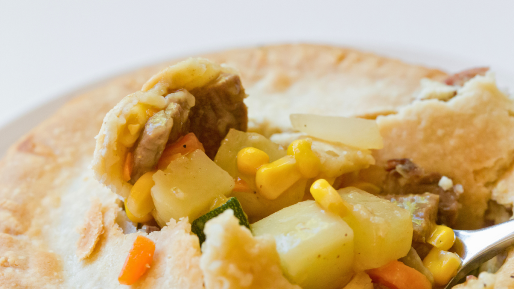 Homemade beef pot pie with flaky golden crust cracked open to reveal tender beef, vegetables, and rich savory filling.