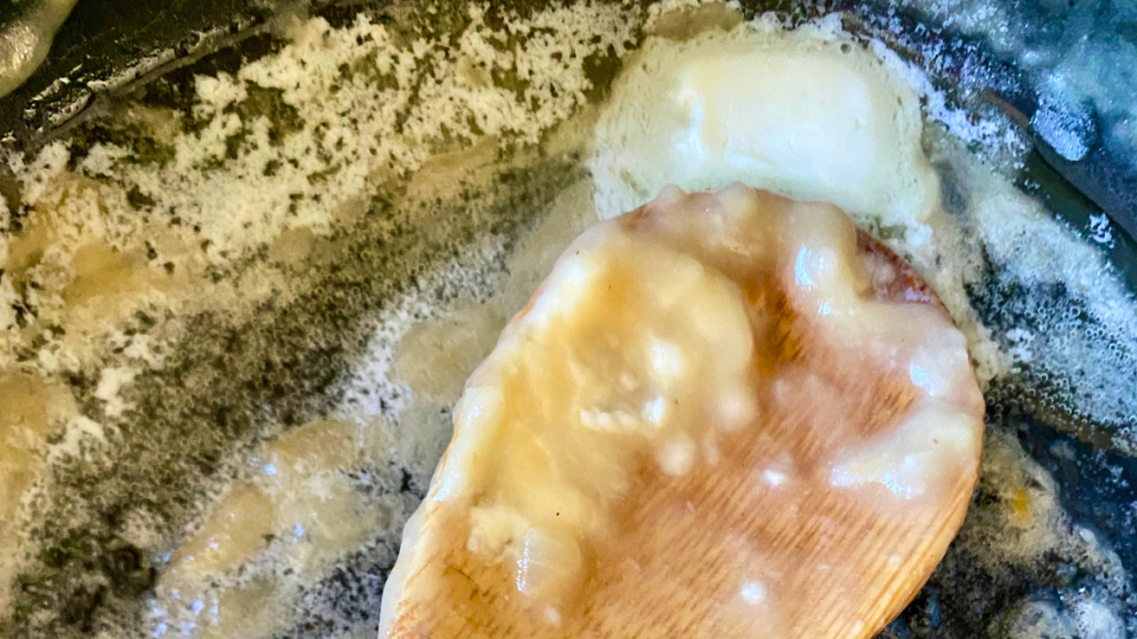 Wooden spoon stirring flour or cornstarch into melted butter in a pan to create the gravy base for homemade beef pot pie.