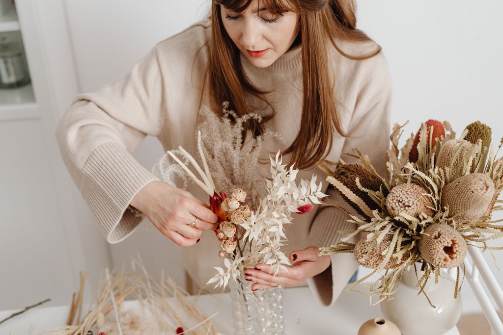 a woman arranging dried flowers indoors for late summer or fall decor