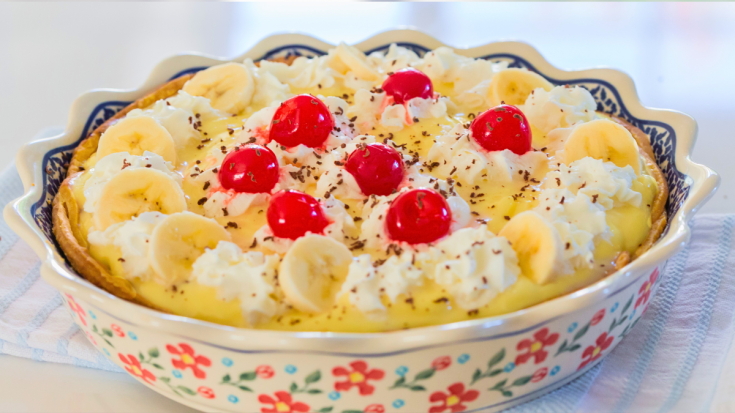 photo of banana split pie closeup in a pastry crust with layers of sliced fruit, sliced bananas, strawberries, and crushed pineapple on a layer of chocolate and garnished with whipped cream cherries.