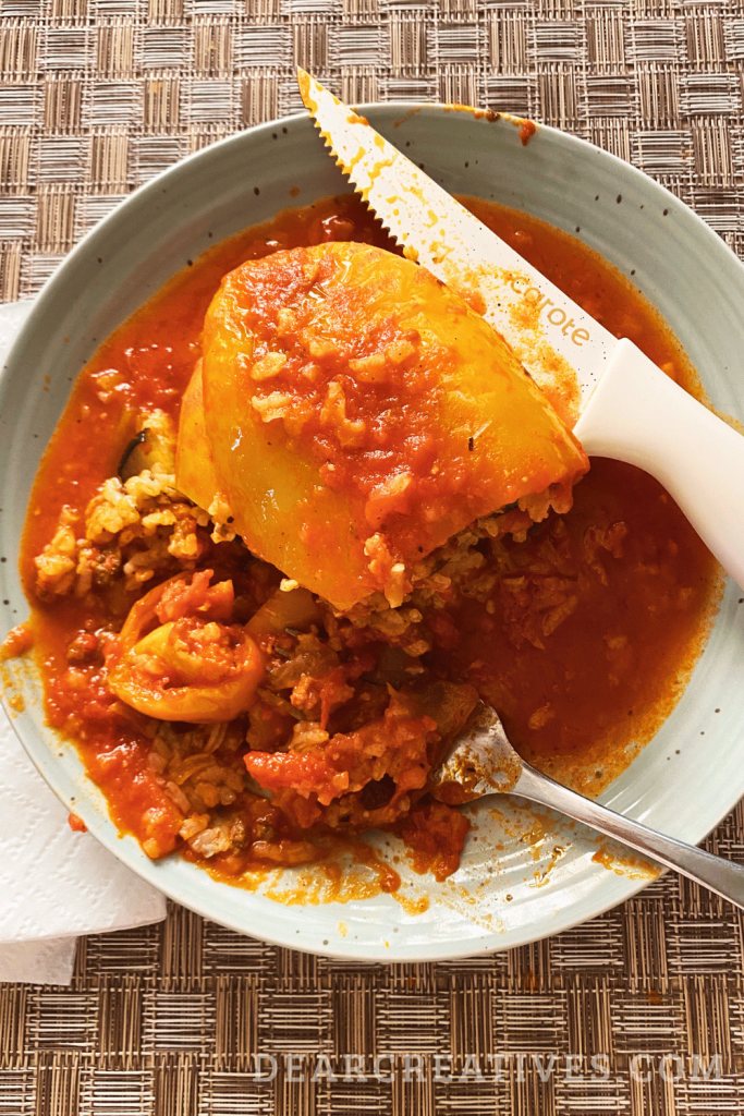 Close up of slow cooker stuffed bell pepper on a plate with rice mixture and marinara sauce being eaten with a fork and knife. 