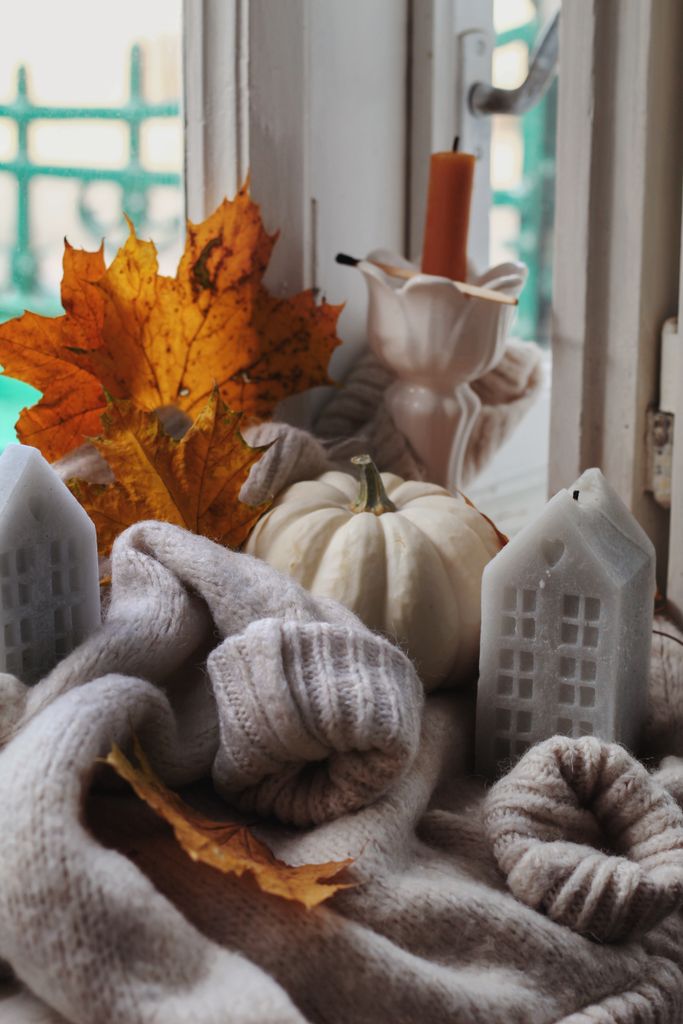 White pumpkin, candles, and fall leaves arranged by a window